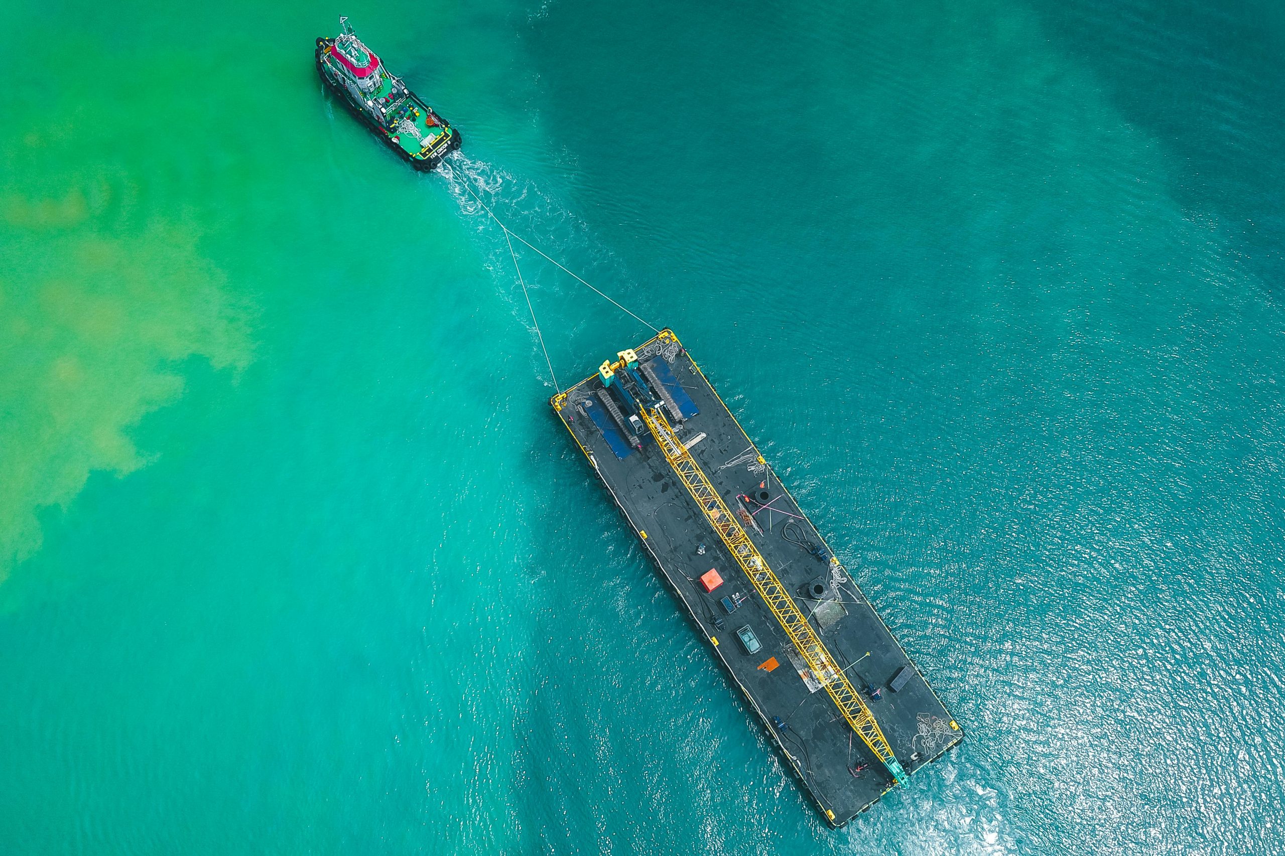 Aerial view of modern powerful motorboat floating on azure seawater and transporting big platform with crane